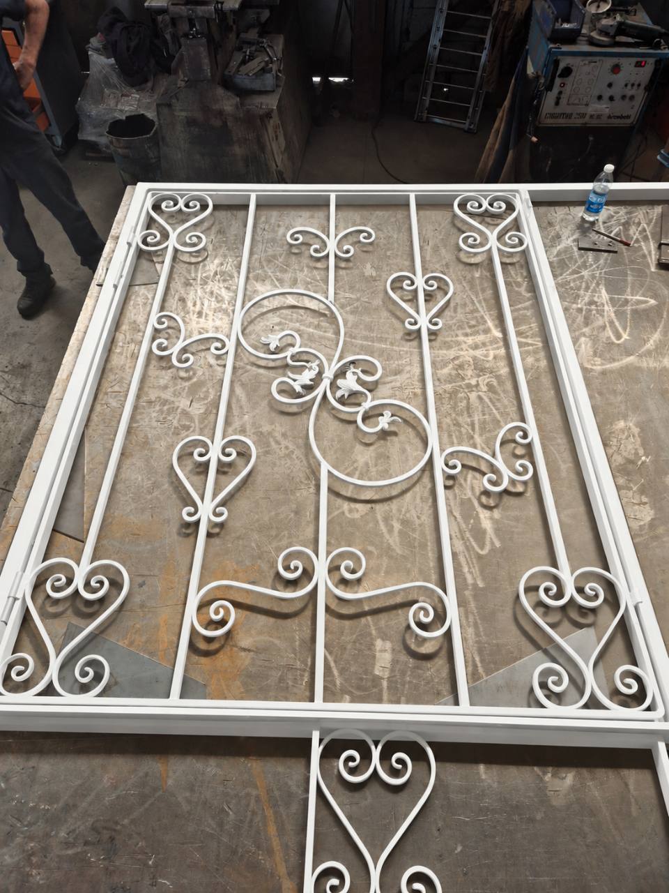 Grille métallique blanche à volutes, présentée sur la table de fabrication.