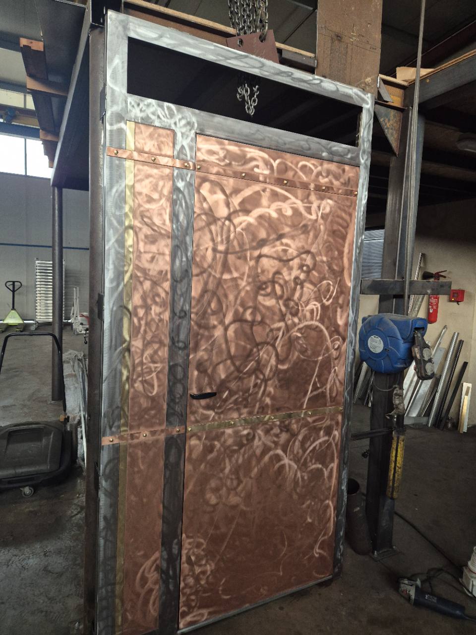 Porte métallique avec habillage en cuivre et bandes décoratives, vue rapprochée en atelier.